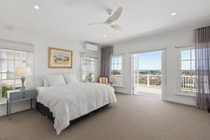 Relax in this serene bedroom with a large bed, nightstand, and lamp, plus a ceiling fan and balcony with a view.