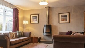 A cozy living room with a fireplace, two sofas, a rug, and framed pictures on the wall. - Our Story Cottage (Alnwick)