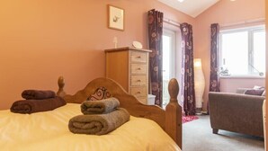 A bedroom with a bed, a wooden dresser, a mirror, a window with curtains, and a sofa. - Our Story Cottage (Alnwick)