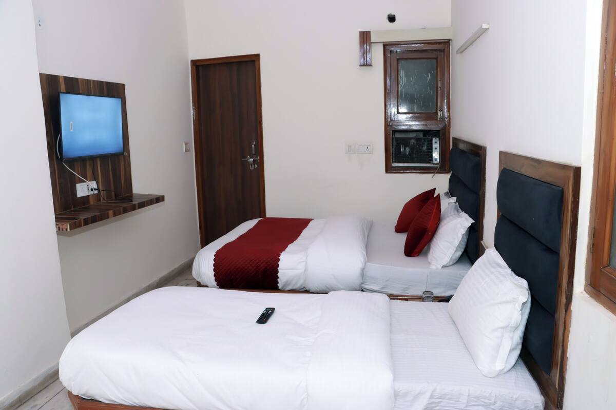 A hotel room with two beds, a TV mounted on the wall, a window with a wooden frame, and a door.