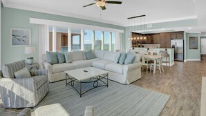 Amplia sala de estar con un sofá modular grande, una mesa de centro y una zona de comedor con una cocina al fondo.