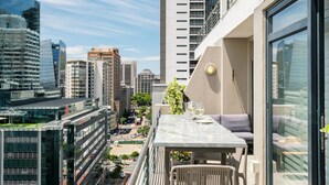Un edificio de gran altura con un balcón que tiene una mesa, sillas y una botella de vino.