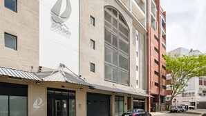 A building with a large sailboat logo on the side, multiple windows, and a parking area with cars. - Cape Town Deluxe City Apartment Hafen Views (Cape Town)
