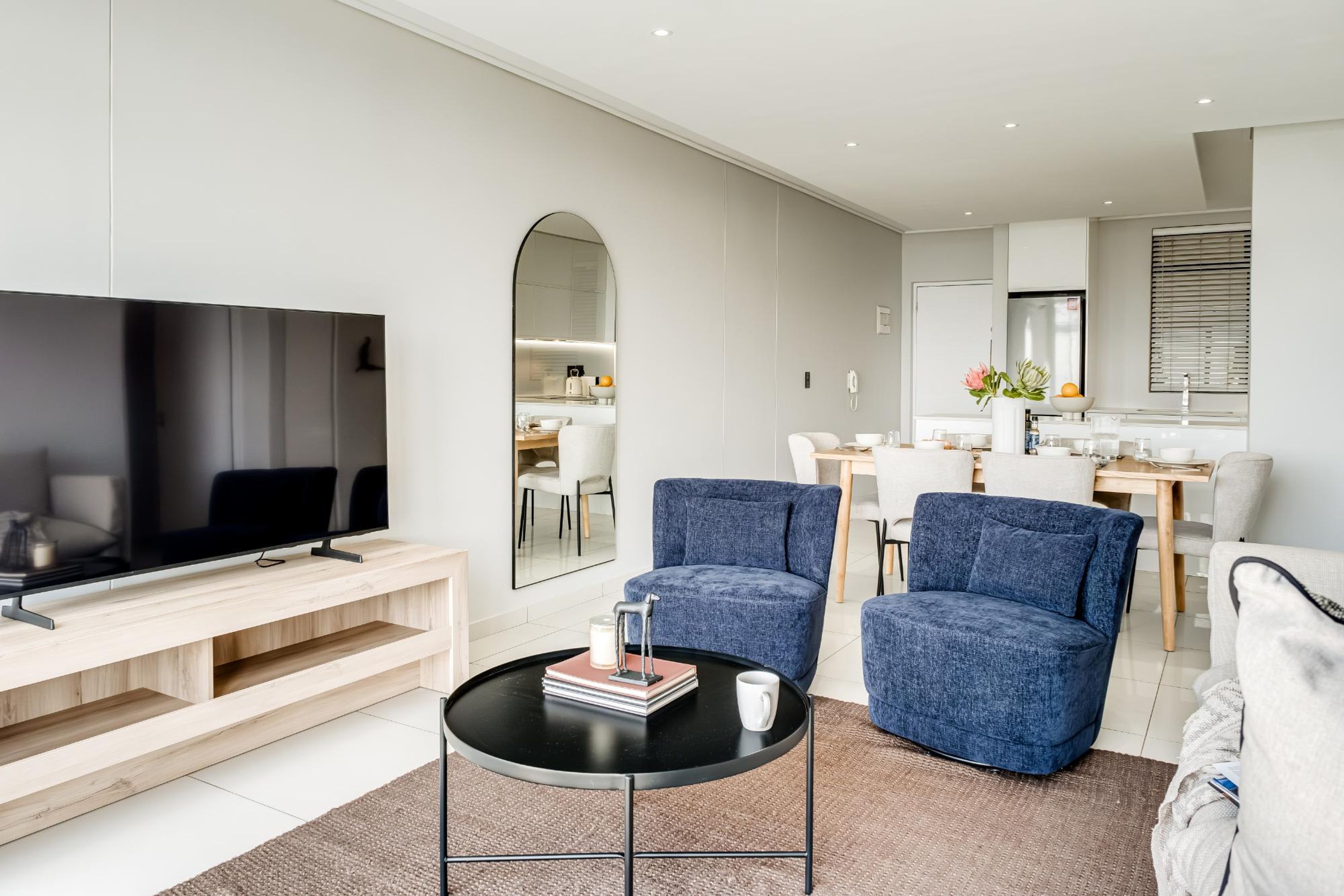 A modern living room with a flat-screen TV, a coffee table, and two blue armchairs.