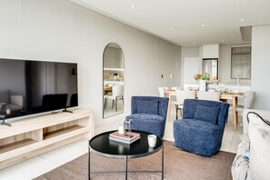Una sala de estar moderna con un televisor de pantalla plana, una mesa de centro y dos sillones azules.