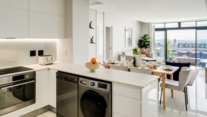 A modern kitchen with built-in appliances, a dining area with a view, and a large window. - Cape Town Deluxe City Apartment Hafen Views (Cape Town)