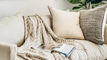 Een gezellige woonkamer met een bank, kussens, een plaid, een plant en een abstract schilderij in een lijst.