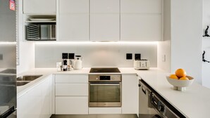 A modern kitchen with white cabinetry, a built-in oven, a dishwasher, and a stainless steel refrigerator. - Cape Town Deluxe City Apartment Hafen Views (Cape Town)