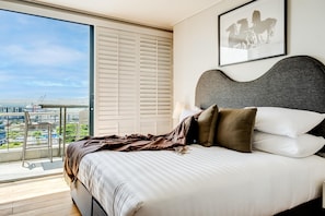 A bedroom with a large bed, a view of the city, and a balcony with a chair. - Cape Town Deluxe City Apartment Hafen Views (Cape Town)