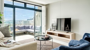 Un moderno salón con televisor grande, asientos cómodos y vista a la ciudad a través de amplios ventanales.