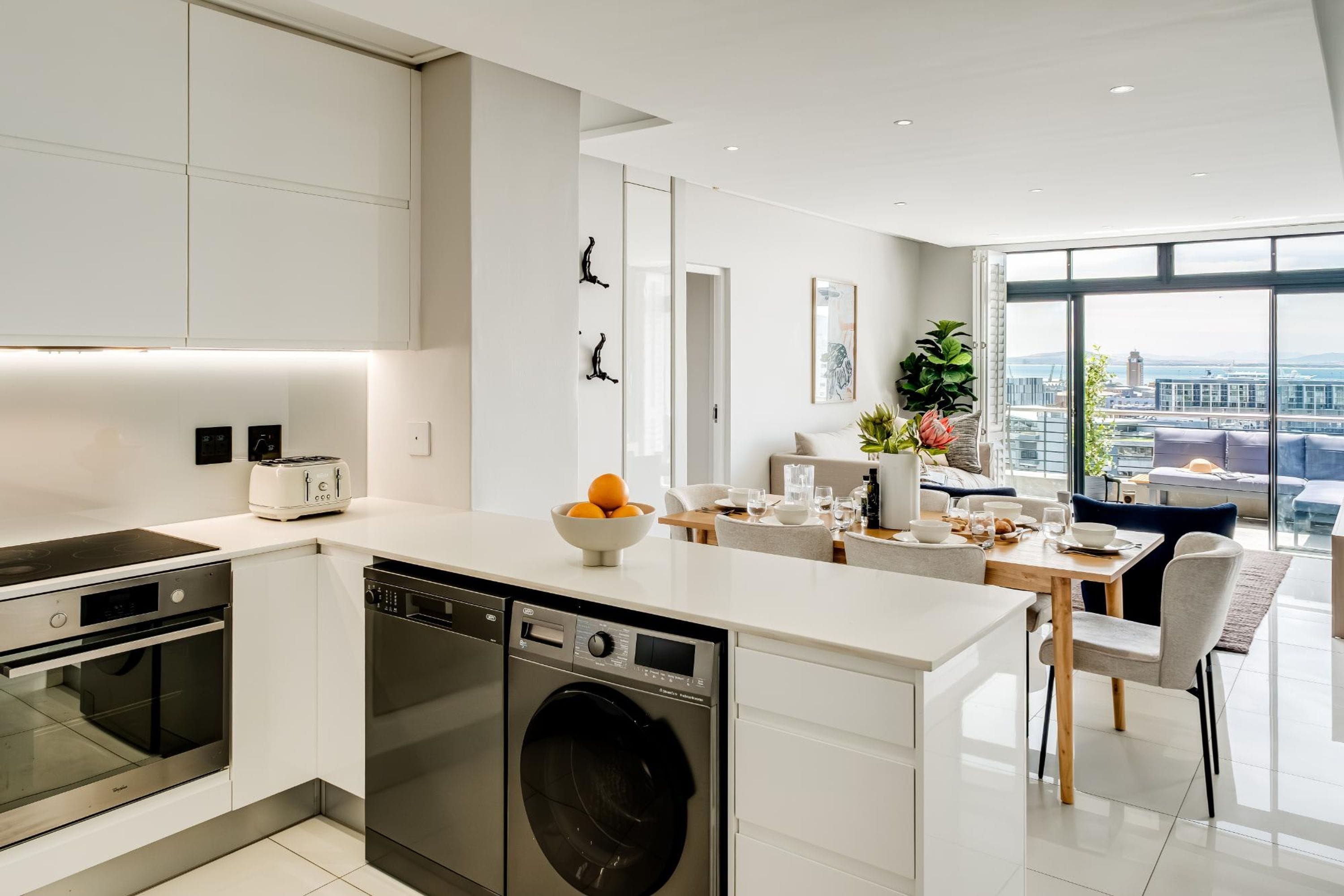 A modern kitchen with built-in appliances, a dining area with a view, and a large window.