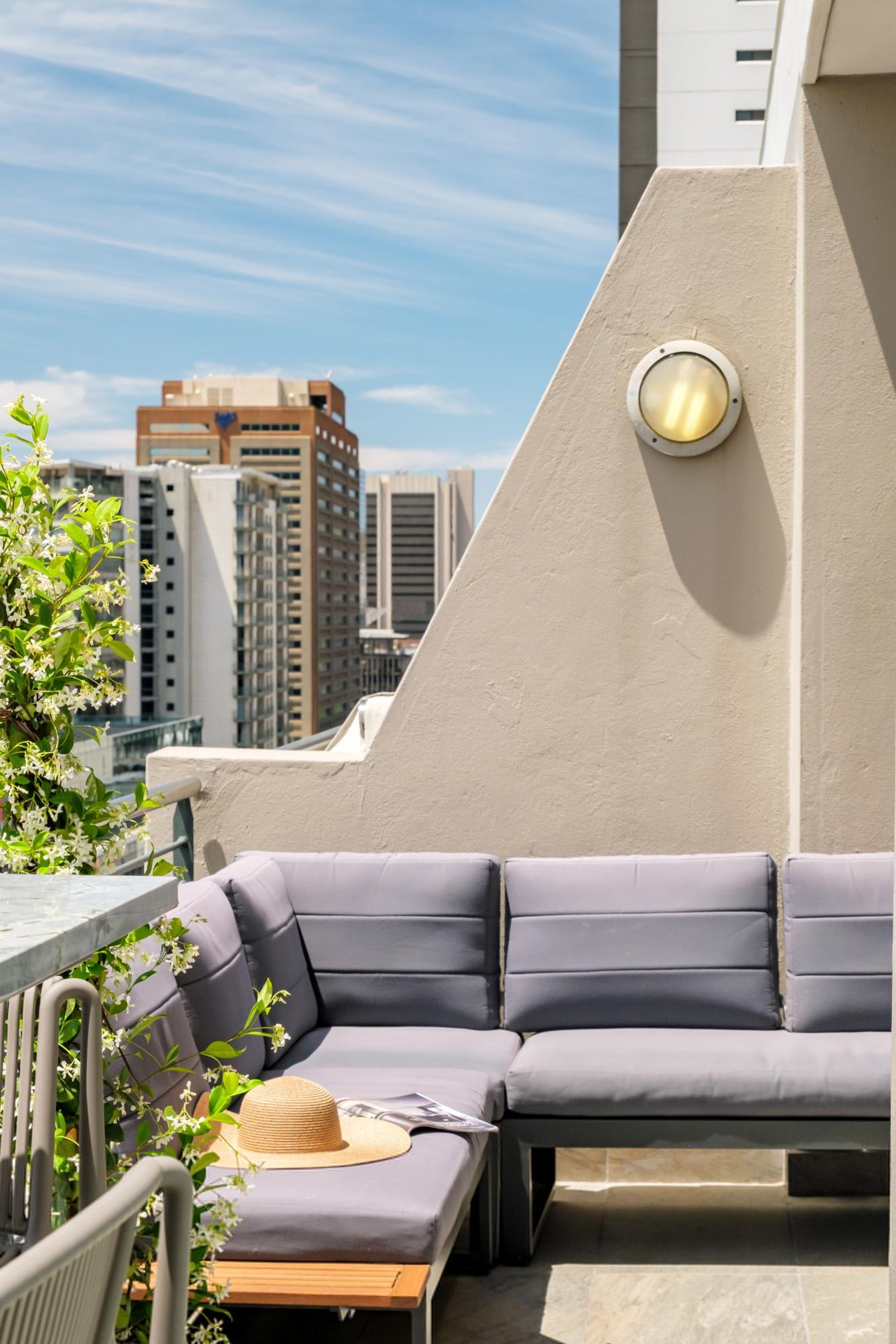 An outdoor seating area with a sofa and a table, a hat, and a window with a view of buildings.