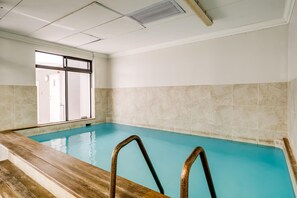An indoor swimming pool with clear blue water, wooden steps, and a tiled wall. - Cape Town Deluxe City Apartment Hafen Views (Cape Town)