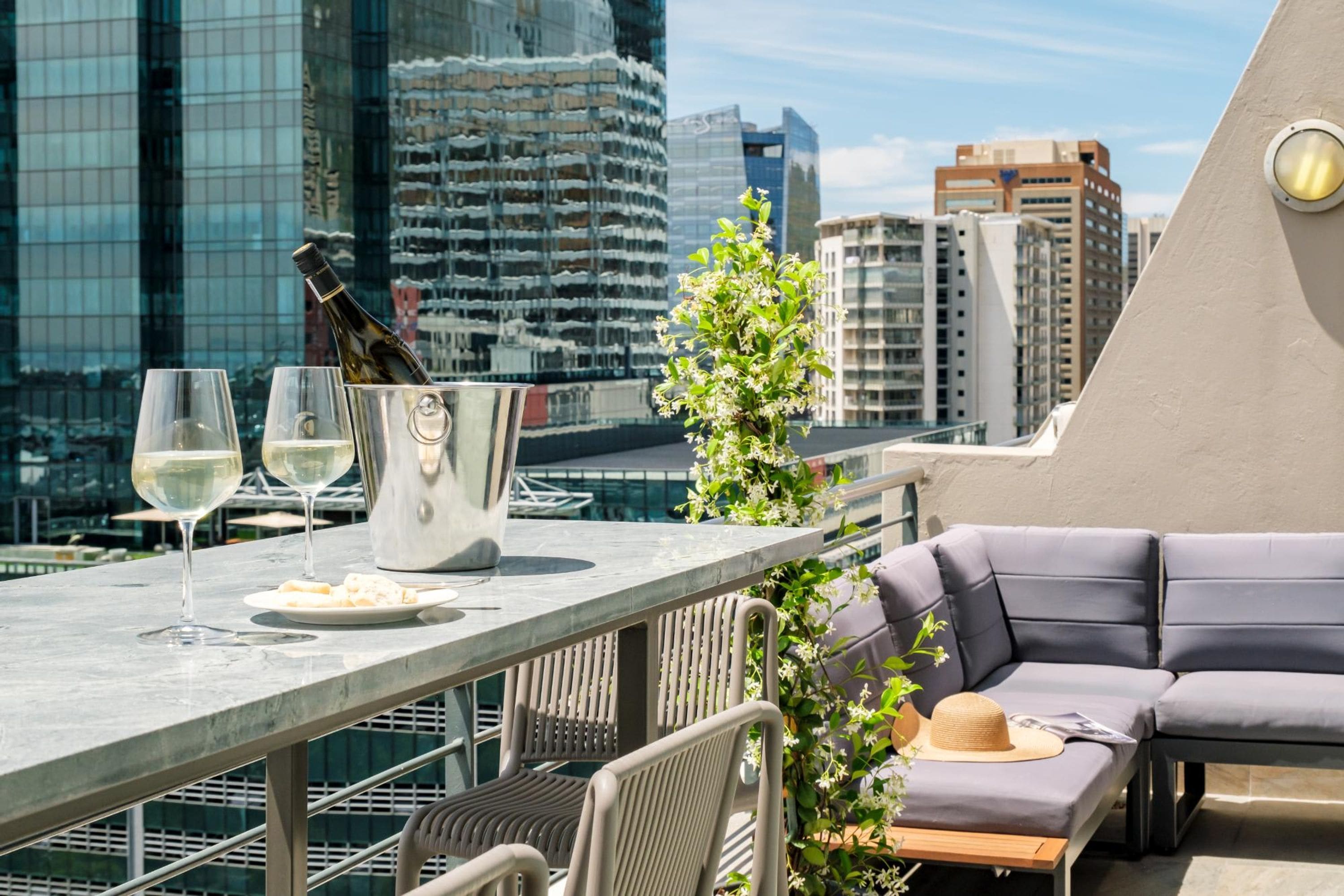 A rooftop terrace with a table set for two, a bottle of champagne, and a glass of white wine.