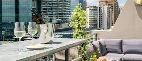 A rooftop terrace with a table set for two, a bottle of champagne, and a glass of white wine.