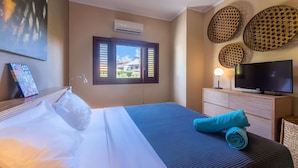 Een hotelkamer met een bed, een televisie, een raam met luiken en decoratieve wandkunst.