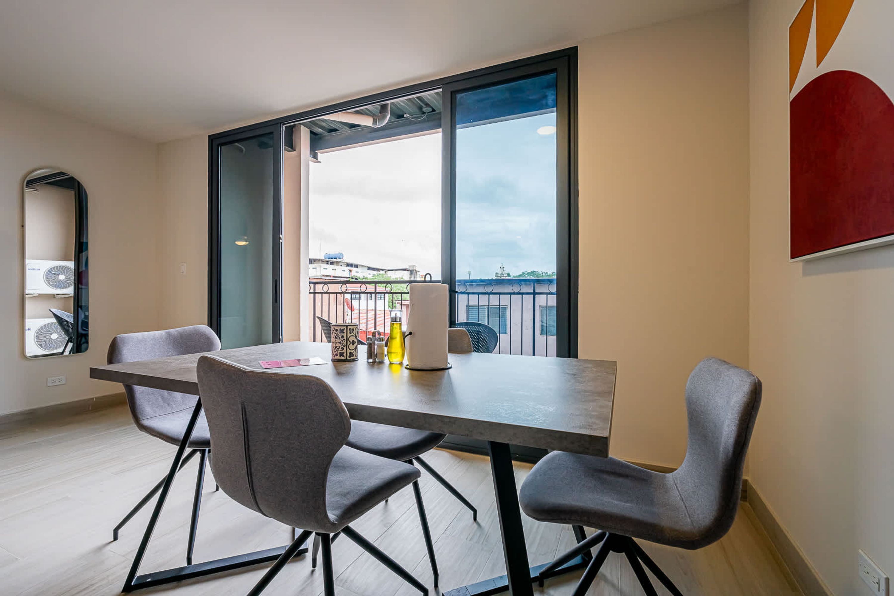 Uma sala de jantar moderna com uma mesa grande, quatro cadeiras e vista para a cidade através de grandes janelas.