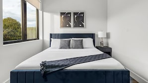 Une chambre d’hôtel moderne avec un grand lit, deux oreillers, une table de chevet avec une lampe et deux œuvres d’art encadrées accrochées au mur.