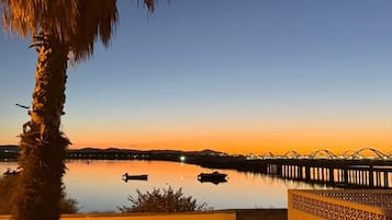 Vista al atardecer con un lago tranquilo, una palmera y un coche estacionado al lado.