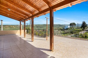 An open terrace with a tiled floor and wooden beams, overlooking a hilly landscape. - Anastasia s House in Drakona (Platanias)