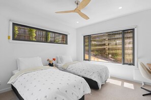 Une chambre avec deux lits, un ventilateur de plafond et de grandes fenêtres donnant sur un jardin.