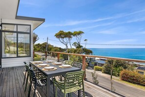 A balcony with a table set for dining, overlooking a coastal view.