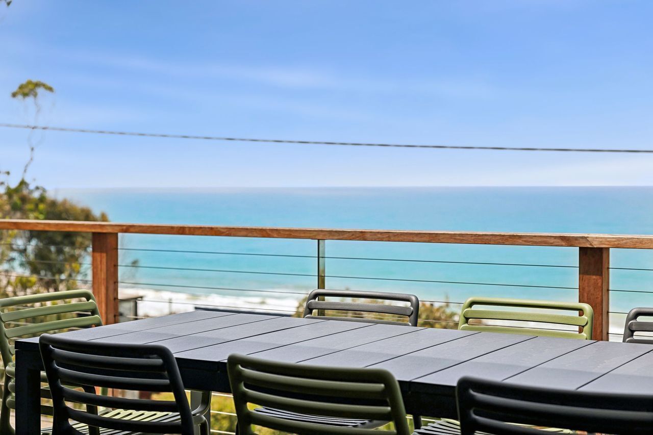 An outdoor dining area with a view of the ocean, featuring a wooden railing and metal chairs.