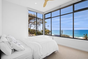 A bedroom with a large window overlooking a beach.