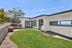 A modern house with a well-maintained lawn, a barbecue area, and a view of the sea.