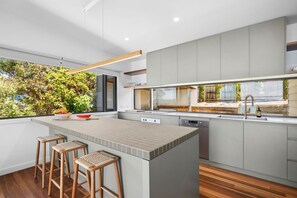 A modern kitchen with a large island, bar stools, and a view of greenery outside.