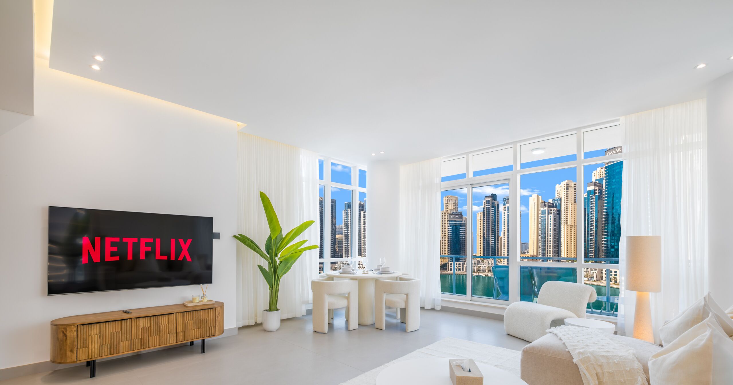 A modern living room with a large TV, a dining area, and a view of a city skyline.