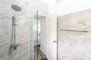 A modern bathroom with a glass-enclosed shower, marble walls, and a visible door leading to another room.