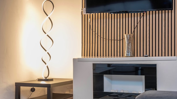 Un salon moderne avec une cheminée, un téléviseur fixé au-dessus, et une lampe décorative en forme de spirale posée sur une table d’appoint.