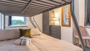 Une chambre avec un lit superposé, un bureau, une chaise et une fenêtre donnant sur un paysage verdoyant.