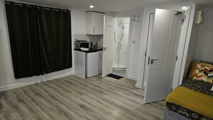 Habitación compacta con kitchenette, zona de ducha y cama.