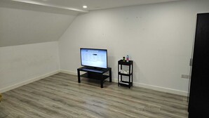 Una habitación con una televisión sobre un mueble bajo, un estante con objetos y una puerta.