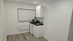 Una cocina compacta con gabinetes blancos, encimera negra, un lavamanos y un microondas.