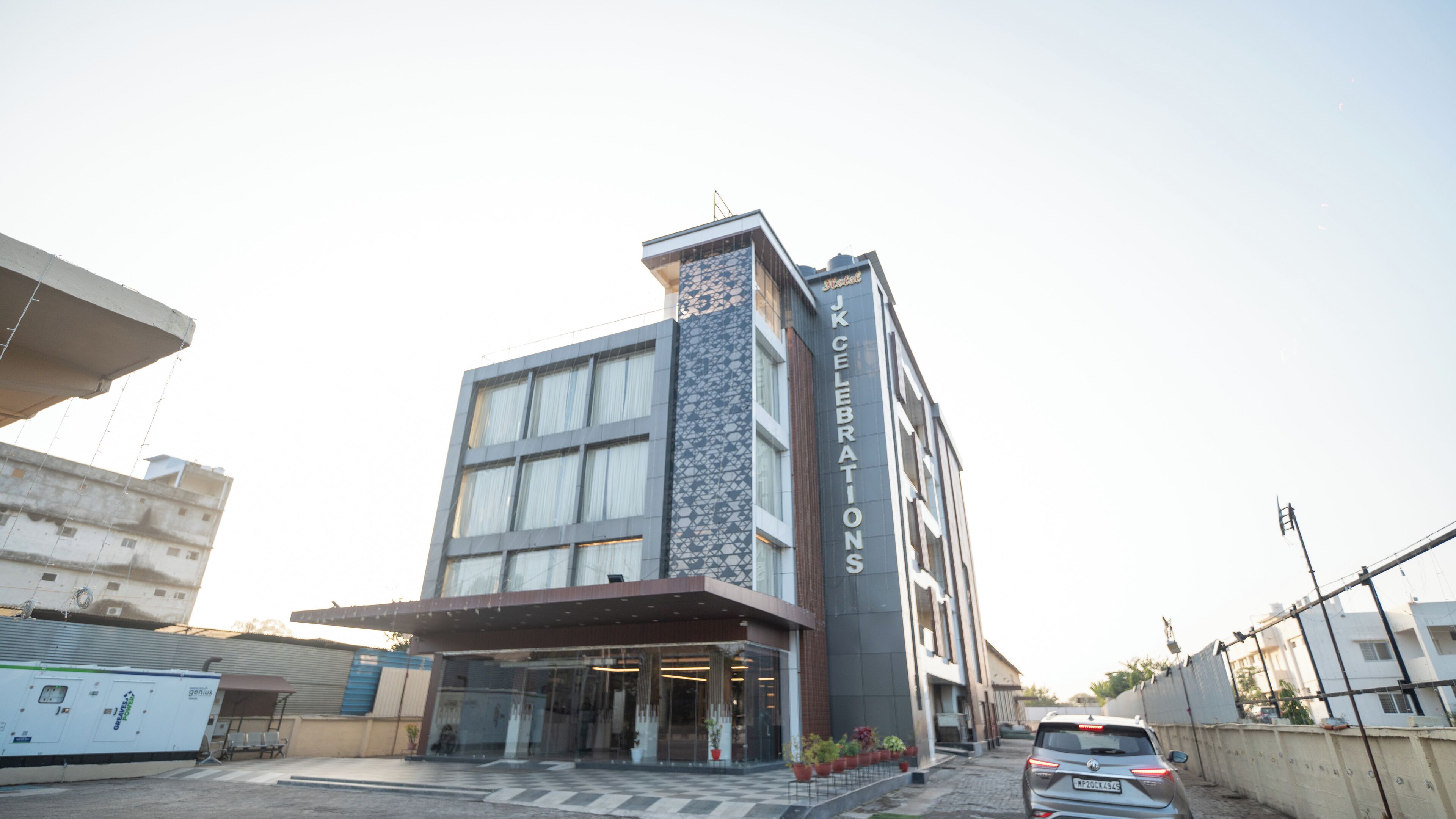 A modern hotel with a prominent 'JKCELEBRATIONS' sign, large windows, and a stone facade.