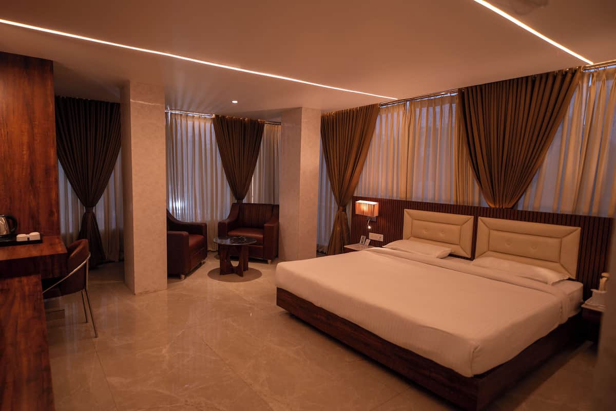 A modern hotel room with a large bed, a desk with a chair, a small table, and a sofa.