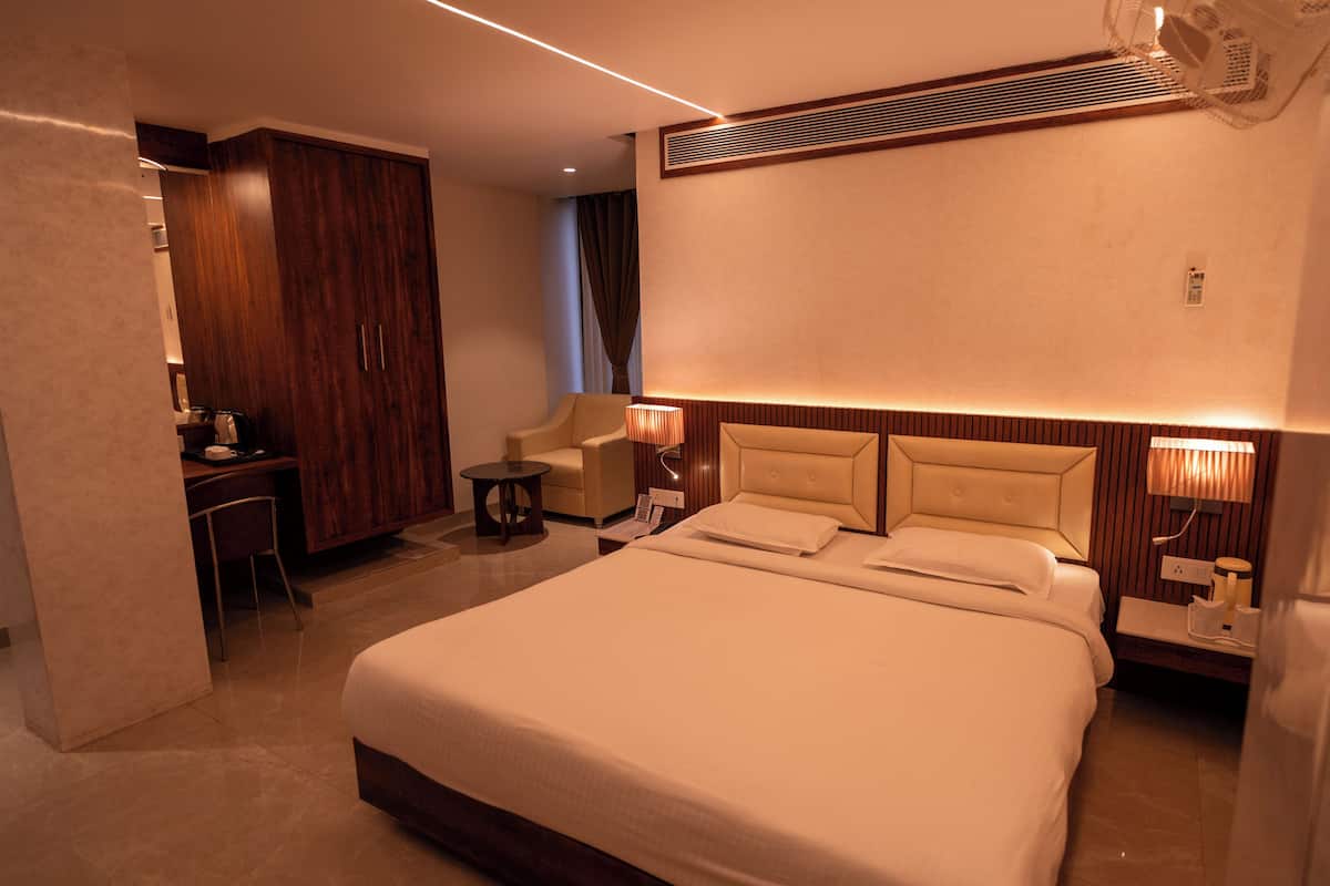 A modern hotel room with a large bed, a desk, a chair, and a wardrobe.
