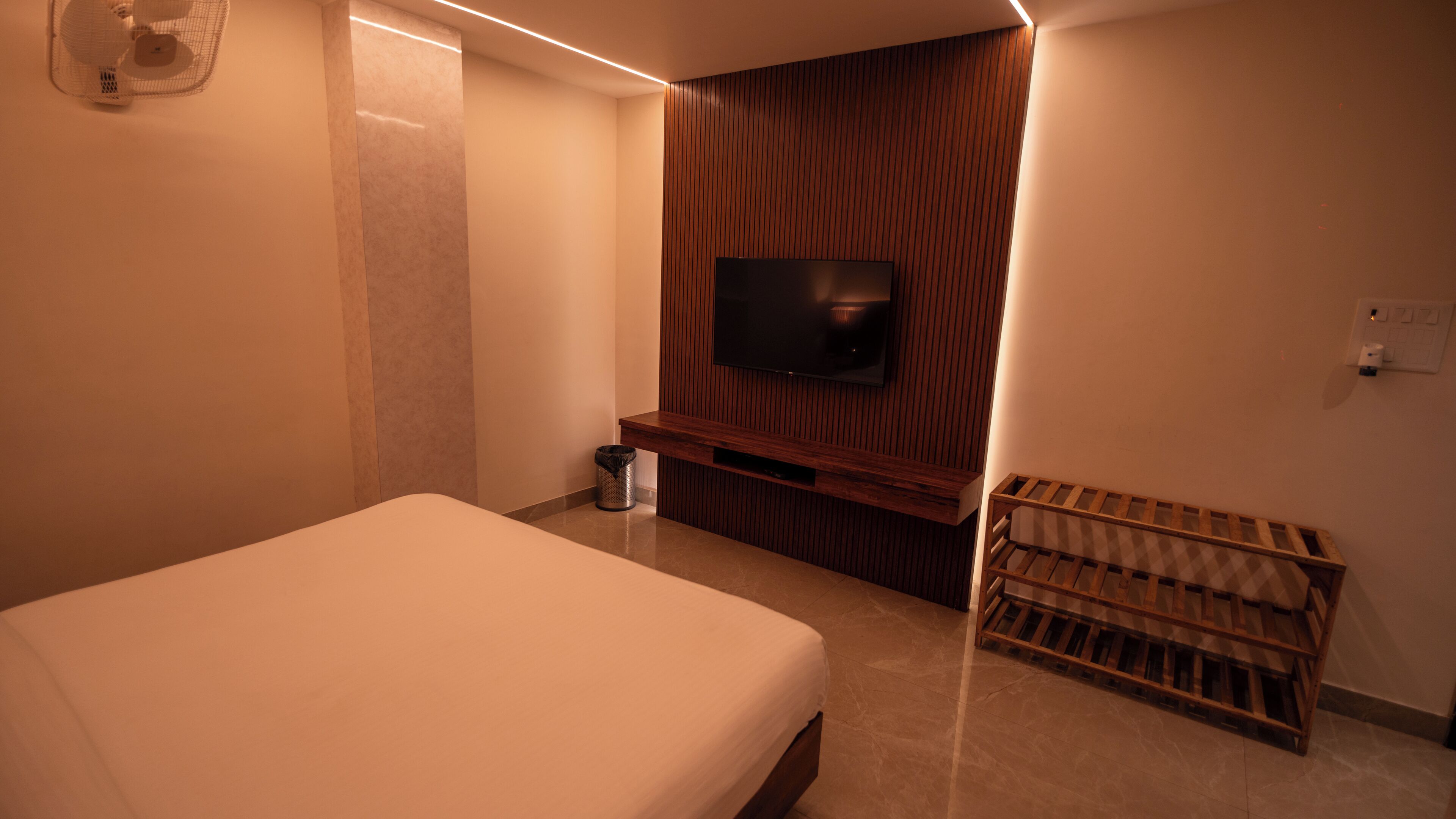 Ein Hotelzimmer mit einem Bett, einem an einer Holzvertäfelung befestigten Fernseher, einem Mülleimer und einer Holzbank.