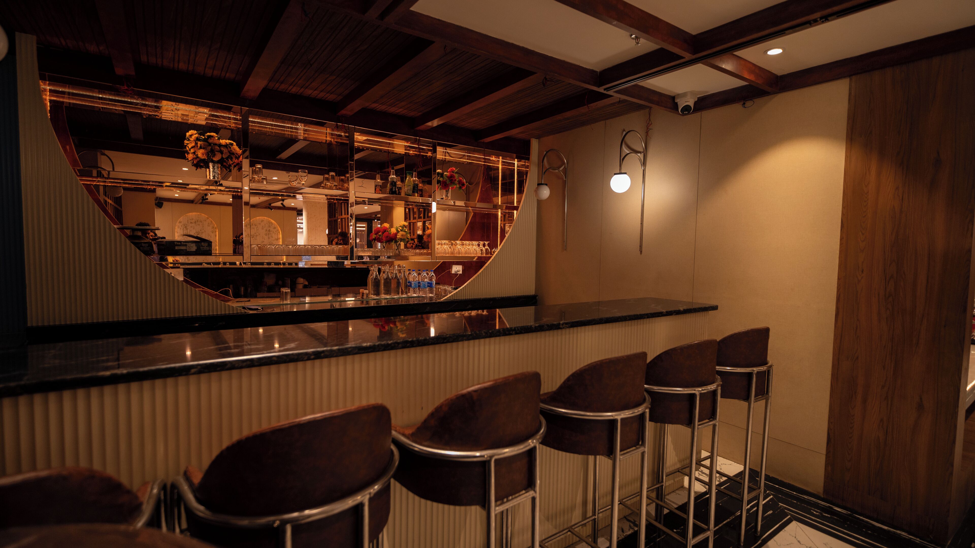 A bar area with a curved counter, bar stools, and a mirrored wall reflecting the interior.