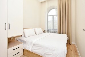 A bedroom with a bed, white wardrobe, and a window with curtains.