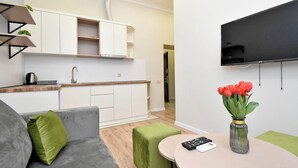 A modern living room with a grey sofa, green cushions, a small round table with a remote control, and a vase with red flowers. - Apartment on Khanjyan street (Yerevan)