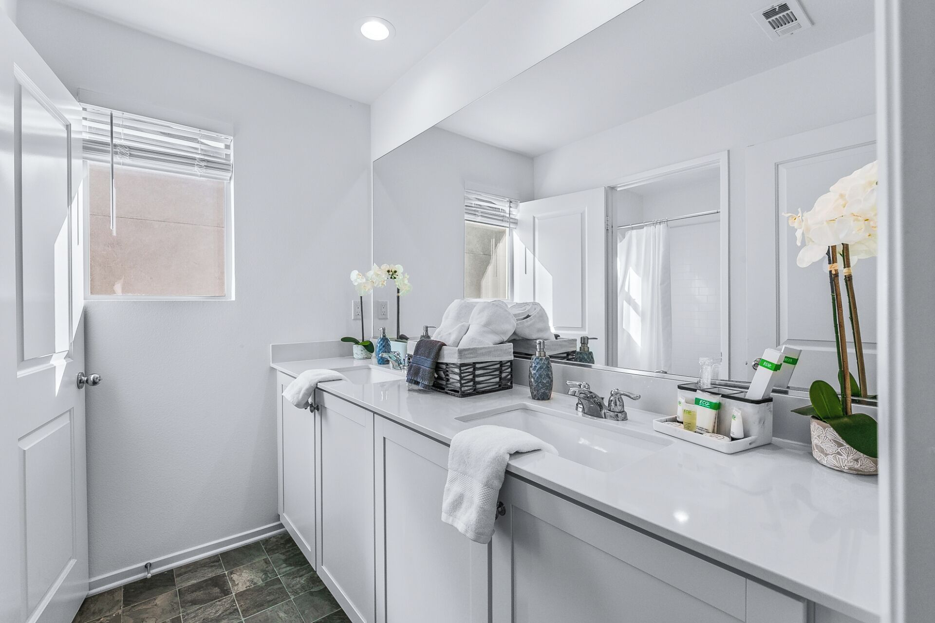 Un bagno moderno con un mobile vanitario bianco, uno specchio grande e una finestra con persiane.
