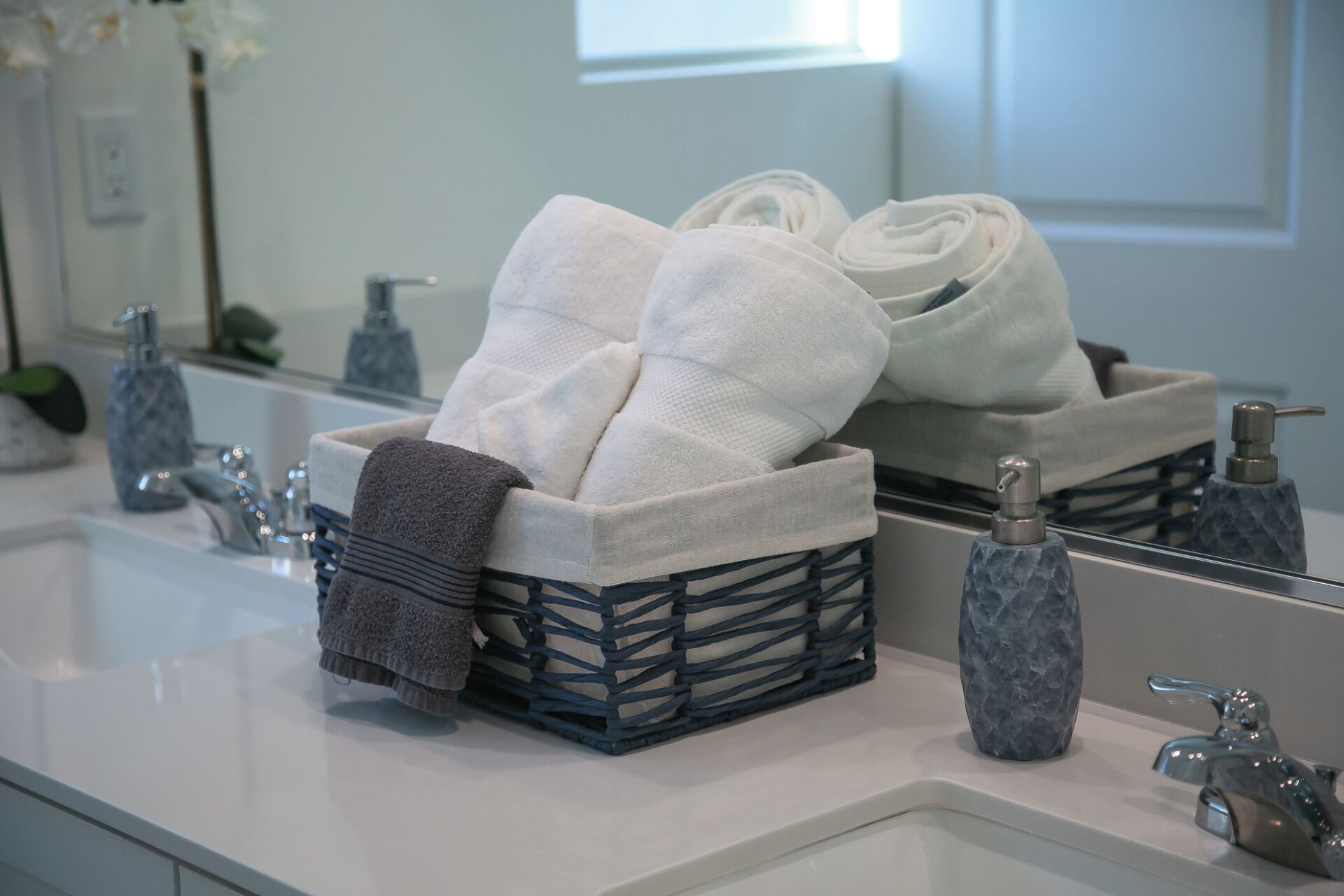 Ein Badezimmer mit einem weißen Waschbecken, einem Spiegel und einem Wäschekorb mit weißen und grauen Handtüchern.