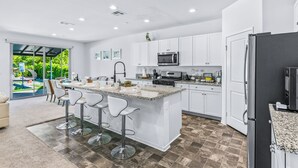 A modern kitchen with white cabinets, a central island with bar stools, a built-in microwave, and a refrigerator.