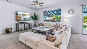 A modern living room with a large flat-screen TV, a ceiling fan, a dining table, and a sofa.