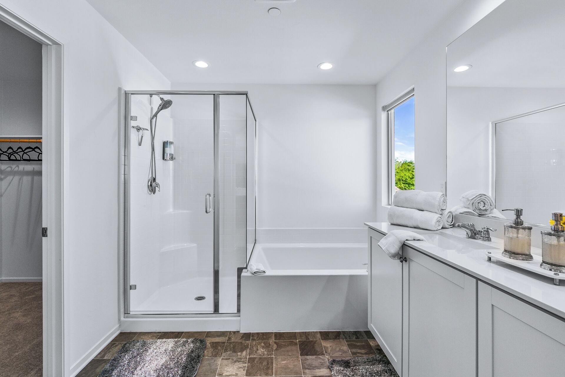 Une salle de bain moderne dotée d’une douche à parois de verre, d’un grand miroir et d’une fenêtre donnant sur la verdure environnante.