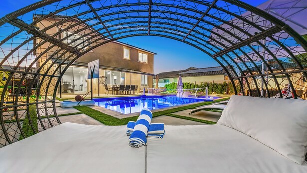 A pool area with a covered seating area and a house in the background.
